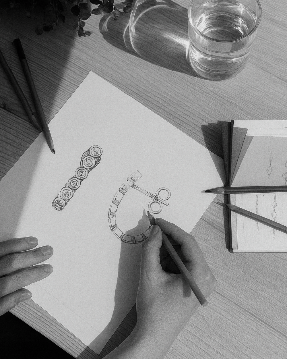 Hånd, der tegner skitse af Eclipse Hoops smykker på papir i ateliermiljø.