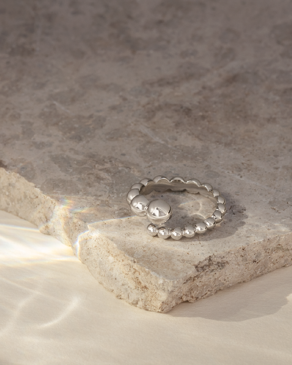 Softpack foto med en Orbis ring i sterlingsølv placeret på travertin sten.