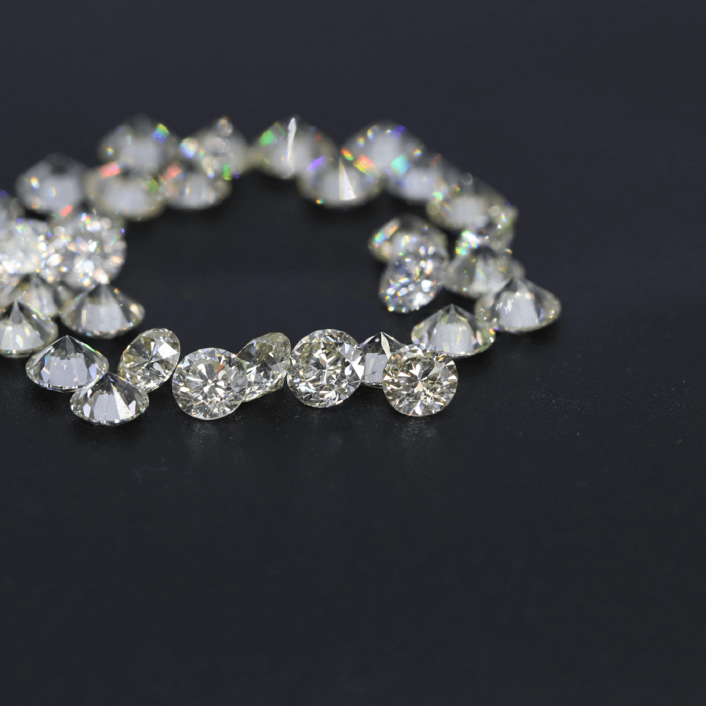 Laboratorieskabte diamanter i rund brillantform lagt i cirkel på mørk baggrund.