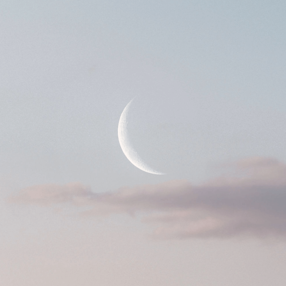 Crescentmåne på lys himmel med bløde skyer i baggrunden.