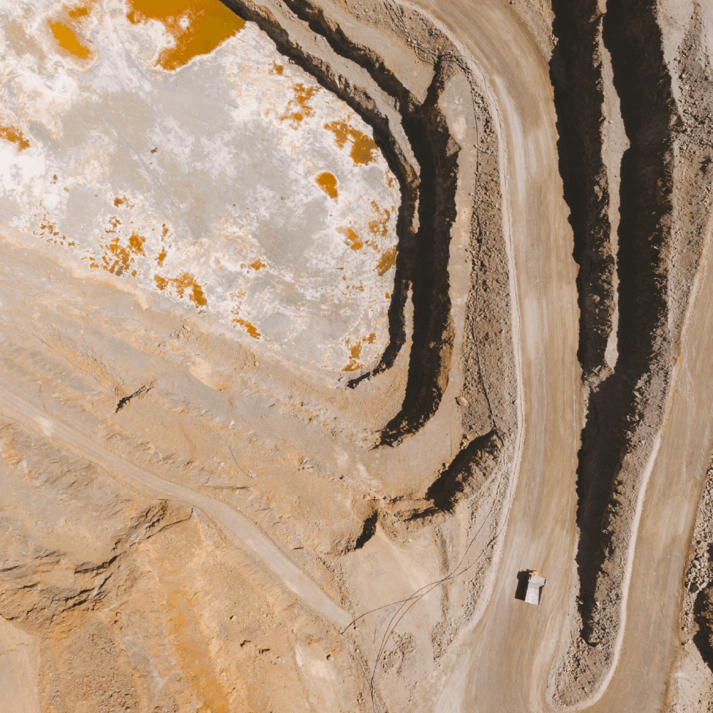 Luftfoto af en råstofudgravning med terrasserede jordlag, stenformationer og lyse mineralaflejringer.