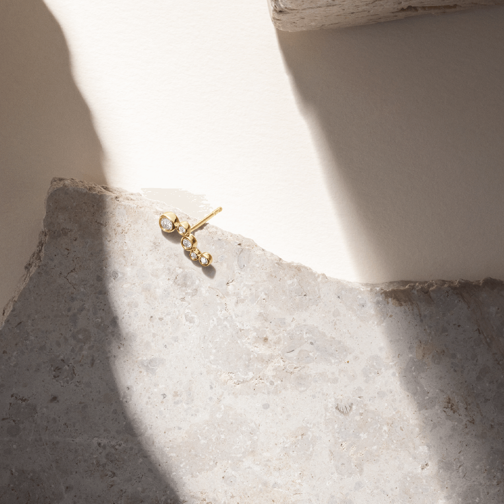 Softpack foto med Eclipse Flow ørering i 14 kt guld placeret på travertin sten.