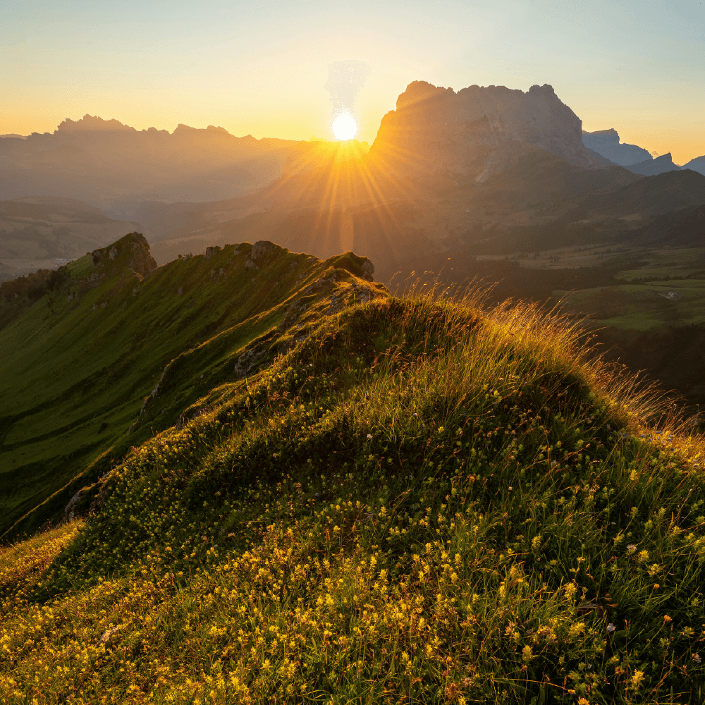Solnedgang over bjerglandskab med varme gyldne stråler, der lyser dale og klippetoppe op.