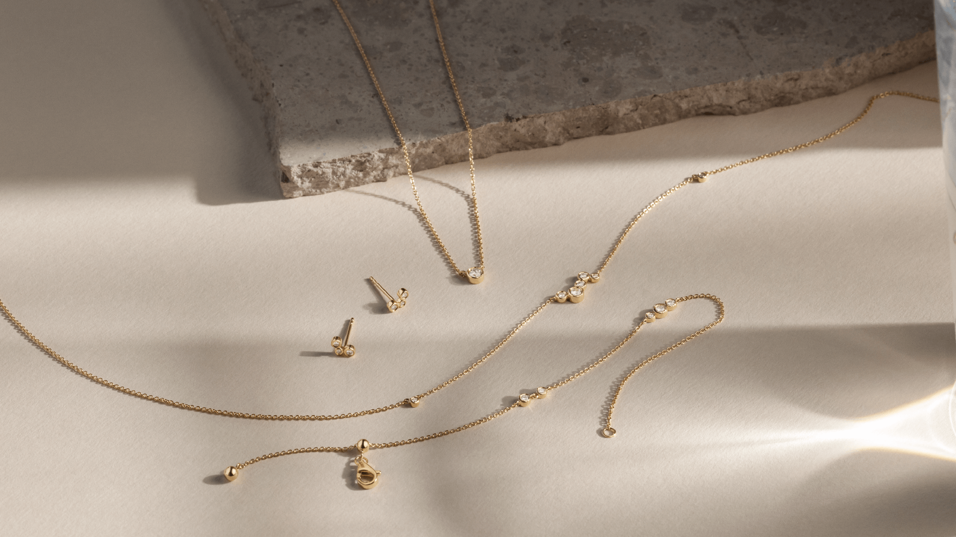 Softpack foto med Eclipse kollektionen i 14 kt guld placeret ved siden af travertin sten.