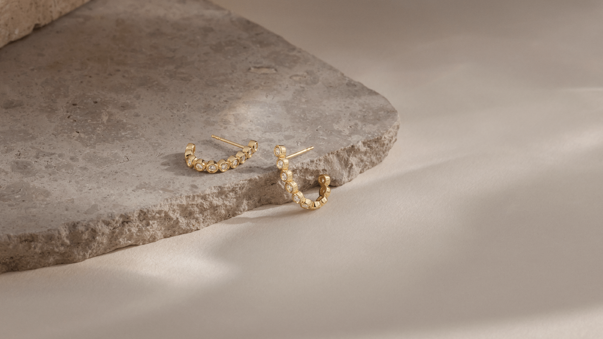 Softpack foto med Eclipse Hoops ørering i 14 kt guld placeret omkring travertin sten.