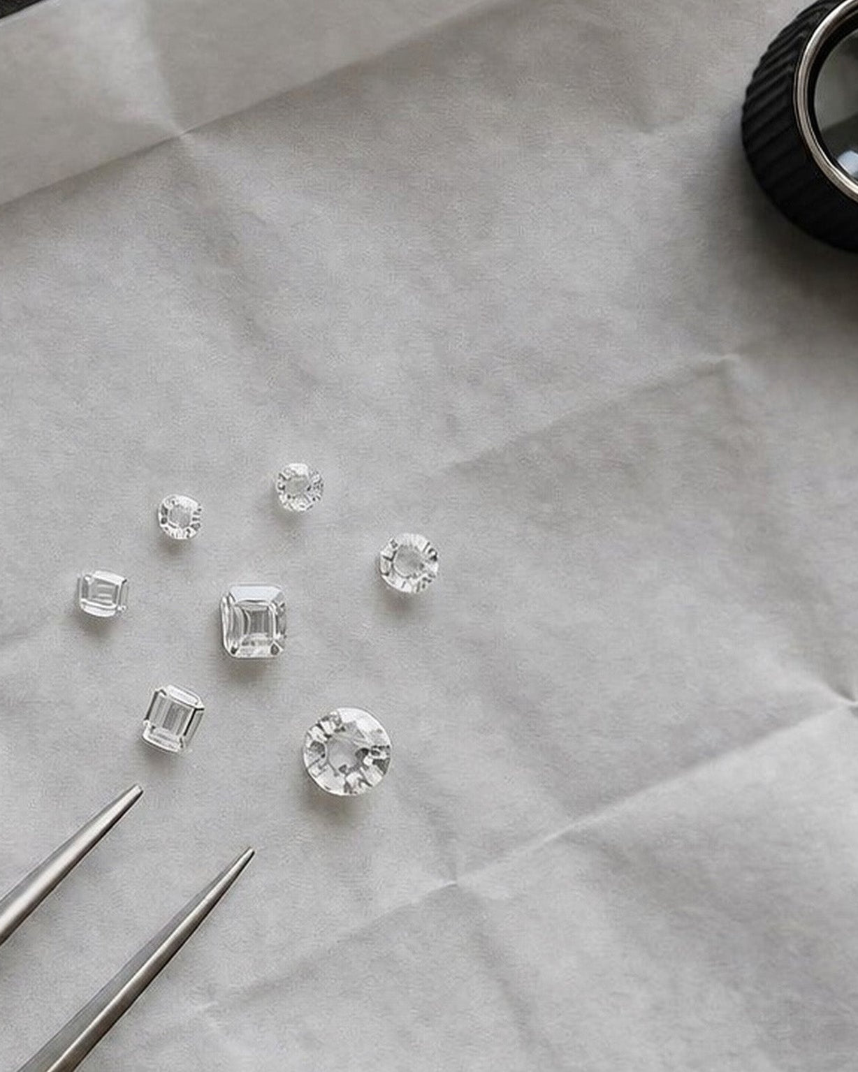 Diamanter på hvidt papir med lup og pincet.