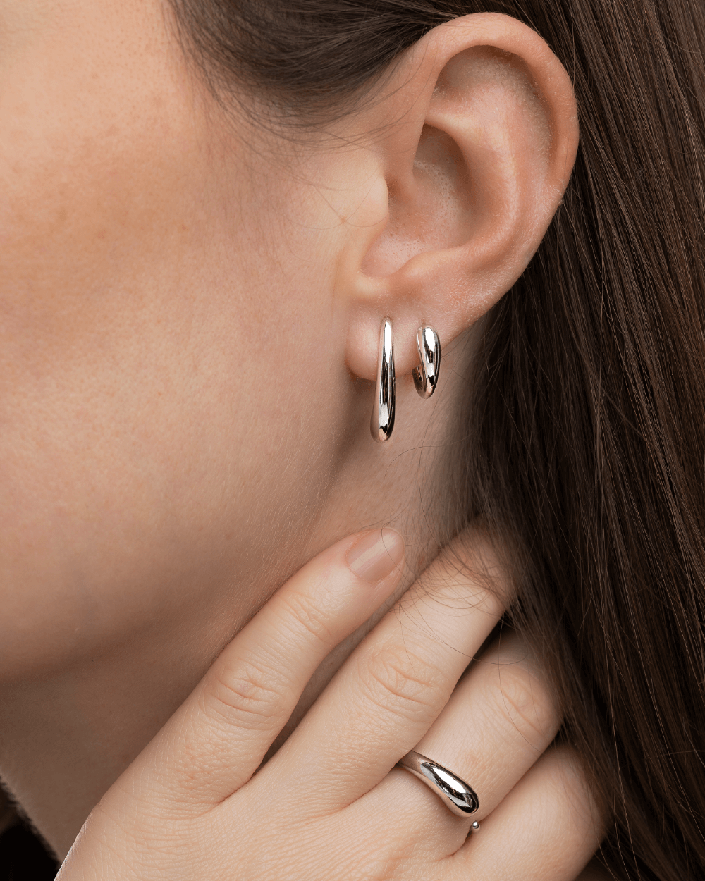 Model med Serene ring og Serene ørering og Serene huggies i sterlingsølv, vist tæt på øre og hånd.