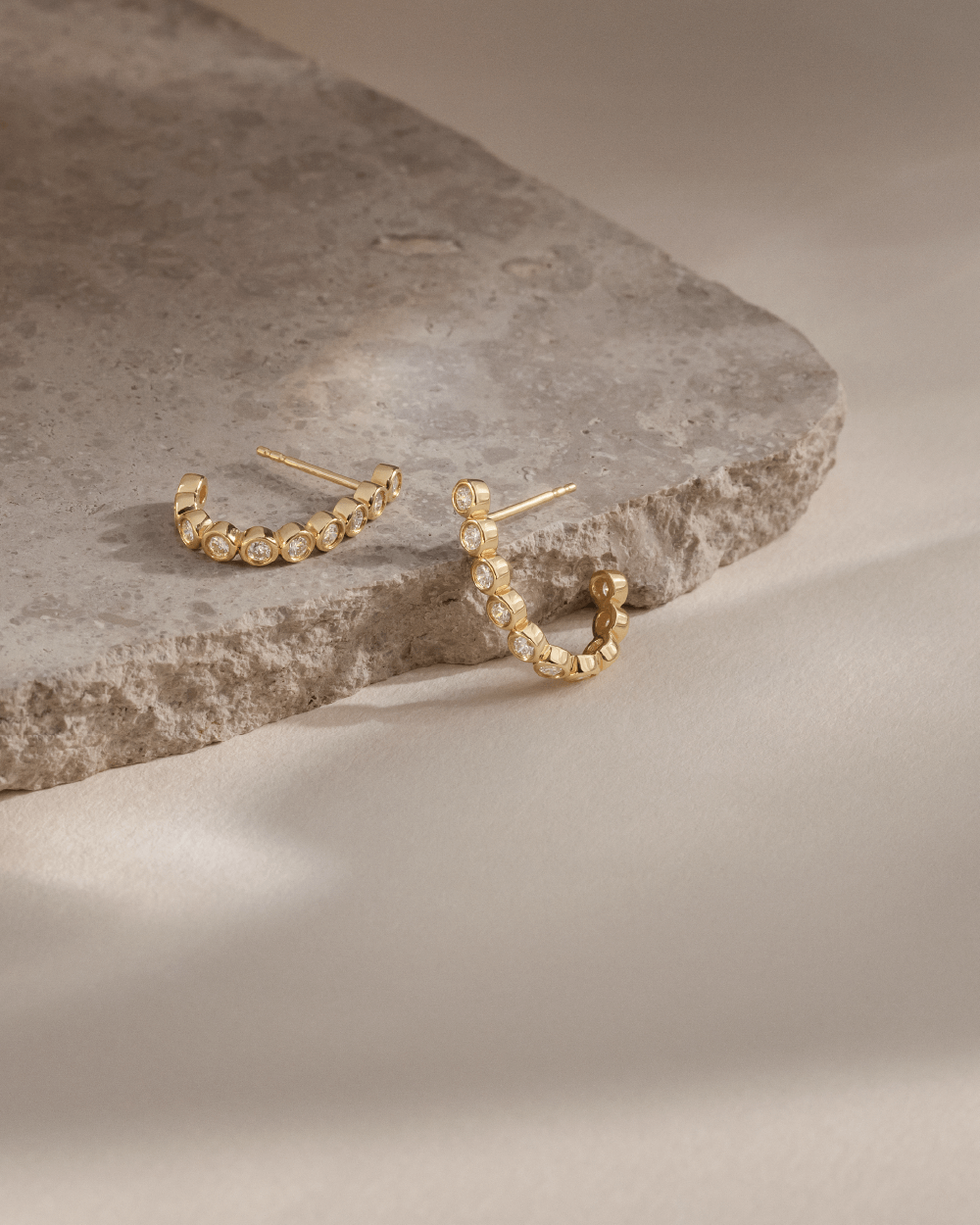 Softpack foto med Eclipse Hoops ørering i 14 kt guld placeret omkring travertin sten.