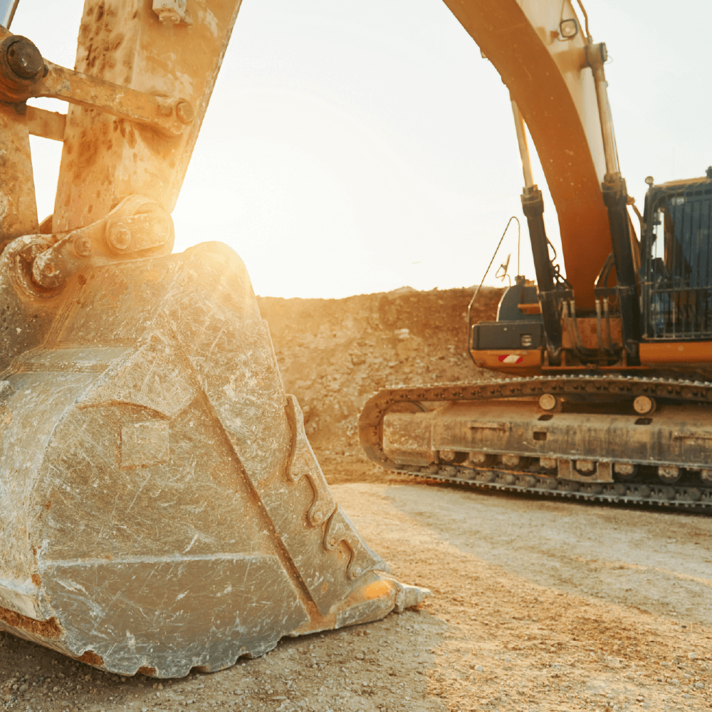 Gravemaskine i sollys under en udgravning, fokus på metalskovl og jord.