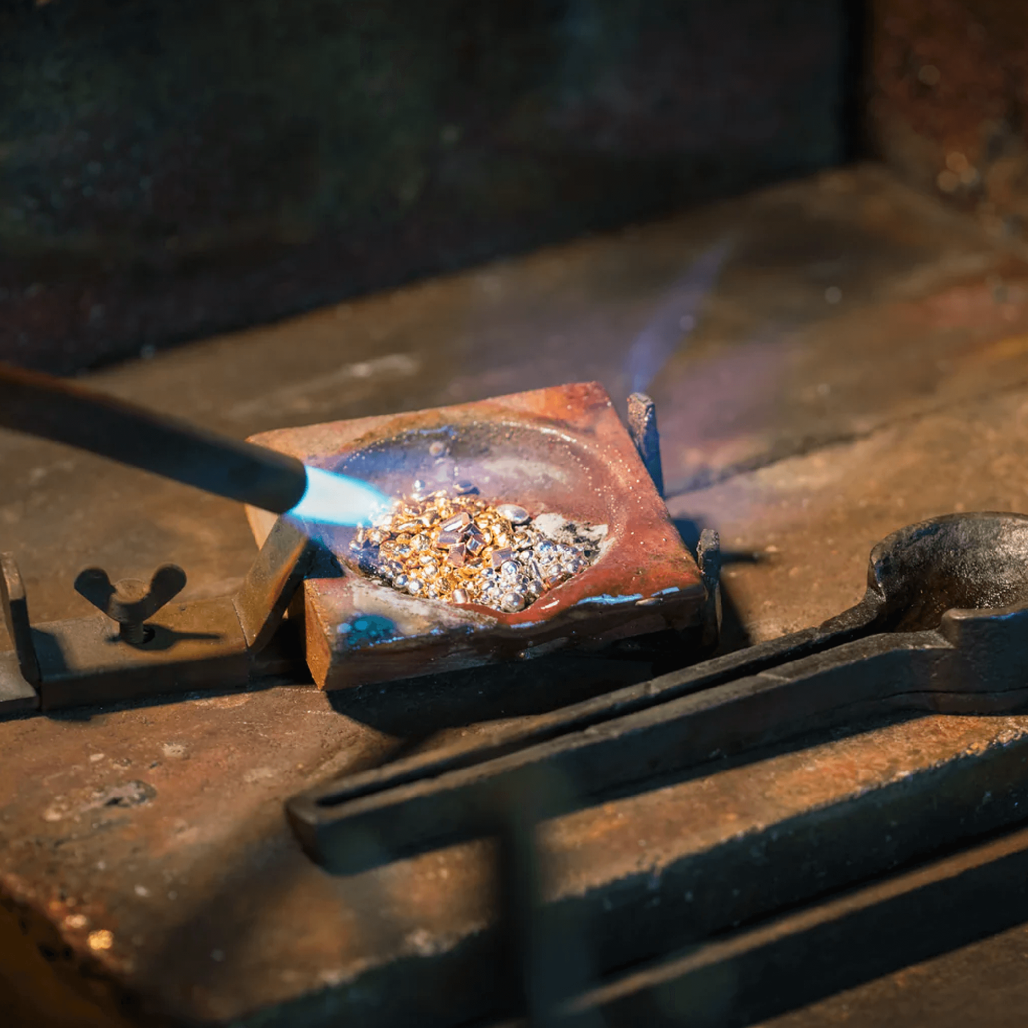 Guld- og sølvgranulater smeltes med flammebrænder i en smelteform under forberedelse til smykkefremstilling.