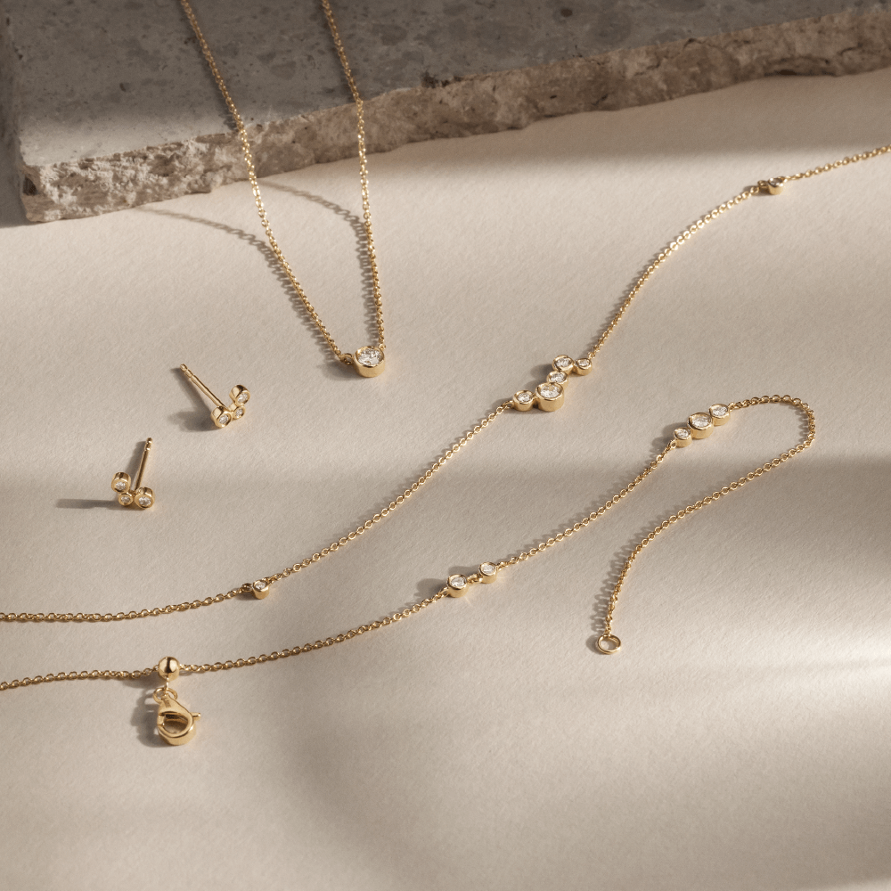 Softpack foto med Eclipse kollektionen i 14 kt guld placeret ved siden af travertin sten.