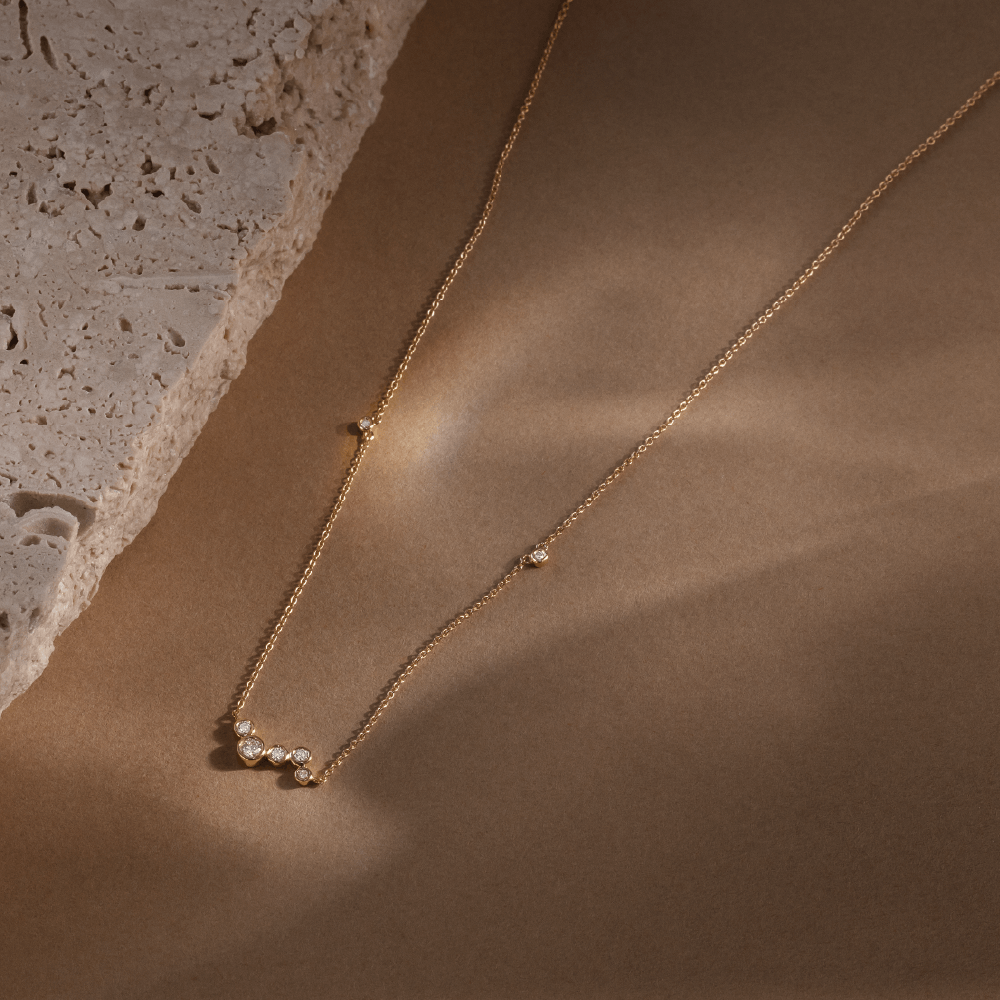 Softpack foto med Eclipse Cluster halskæde i 14 kt guld på brun baggrund med travertin sten ved siden af.