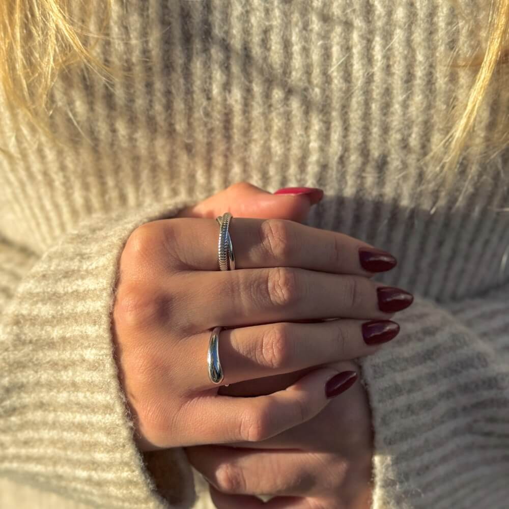 Sølvringe stylet på hænder med rød neglelak op mod lys striktrøje.