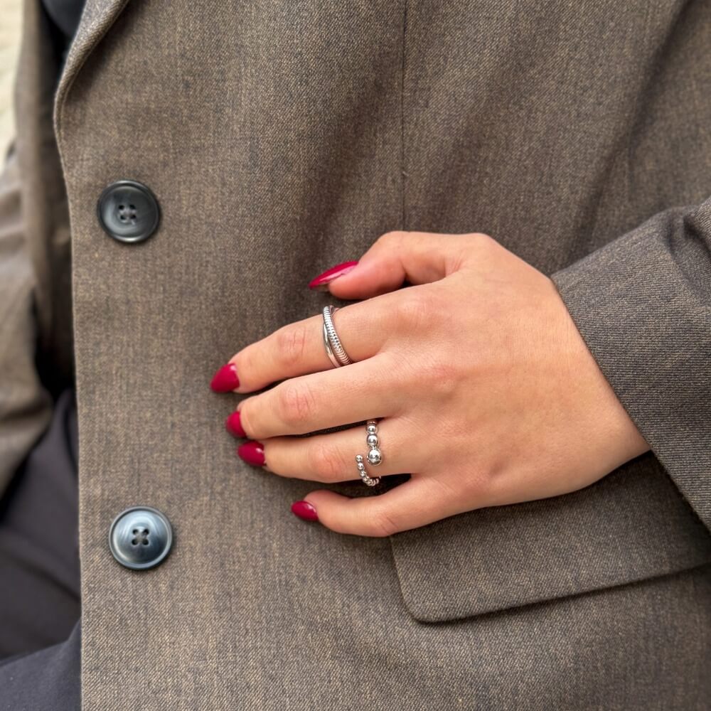 Stabling af sterlingsølv ringe stylet på hånd mod brun blazer.