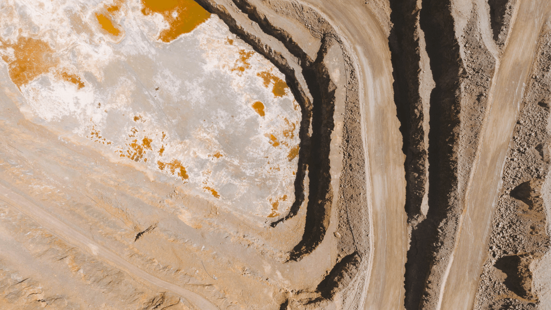 Luftfoto af en råstofudgravning med terrasserede jordlag, stenformationer og lyse mineralaflejringer.