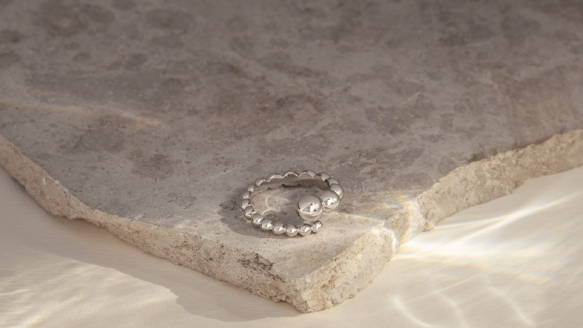 Softpack foto med en Orbis ring i sterlingsølv placeret på travertin sten.