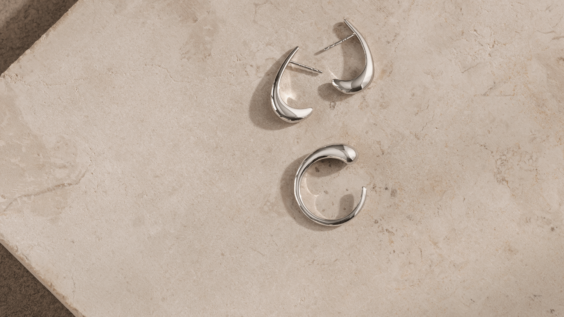 Softpack foto med Serene øreringe og Serene ring i sterlingsølv placeret på travertin sten.